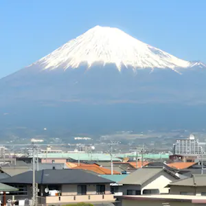 Mount Fuji rises in the distance behind the rooftops of a Japanese town.