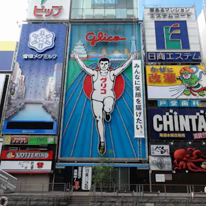 Neon signs at daytime in Dotonbori, Osaka, showing famous Glico athlete with hands raised, surrounded by other colorful signs.