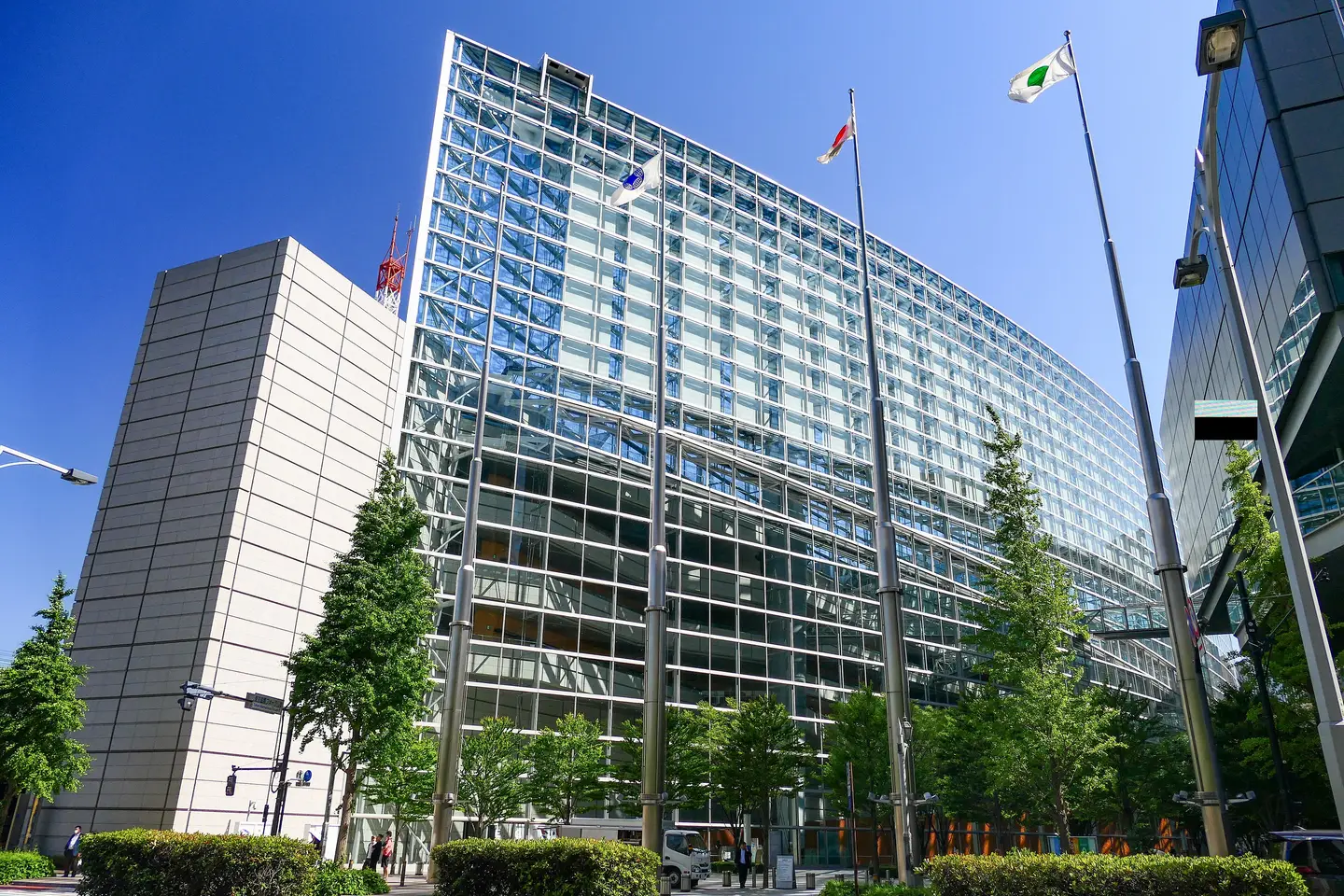 The glass facade of Tokyo International Forum from the street, with trees and flags in front